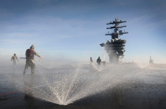 Sailors participate in a countermeasure wash down on the flight deck of the aircraft carrier USS Nimitz