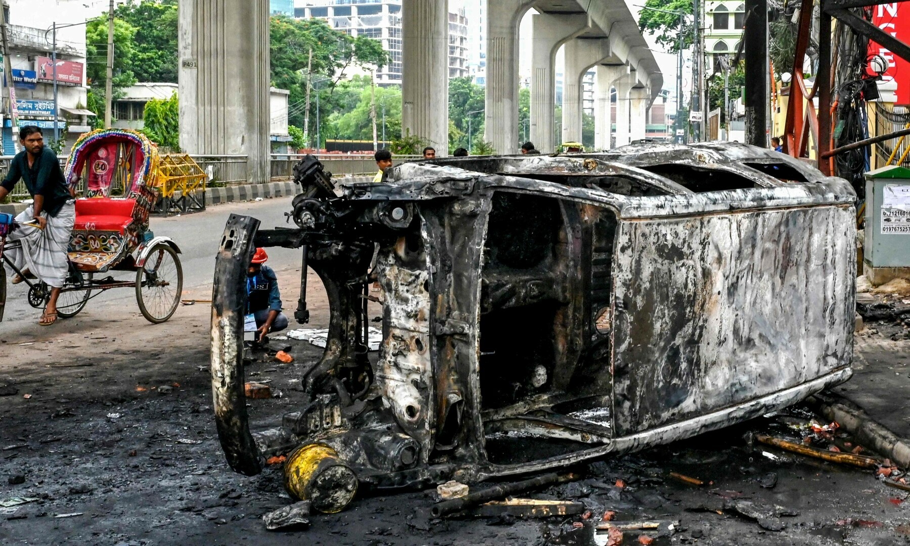 Passersby look at a burnt vehicle along a street amid anti-government protests in Dhaka on August 5, 2024. — AFP