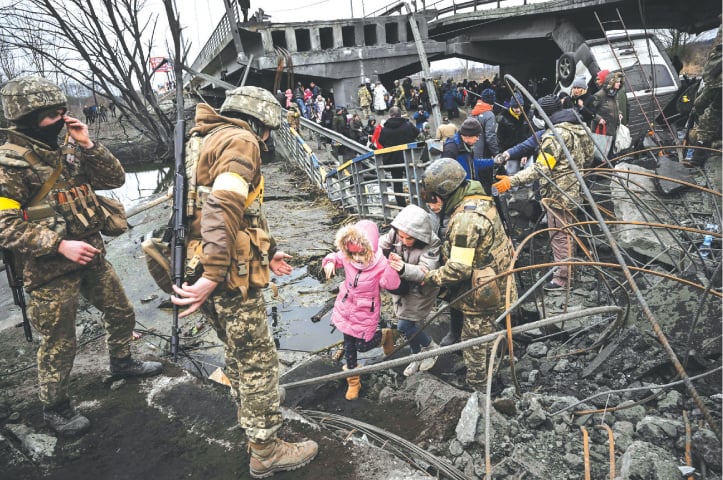 KYIV: People cross a destroyed bridge as they leave the city of Irpin during heavy shelling and bombing on Saturday.—AFP