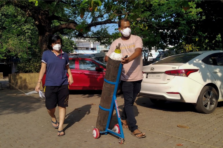 A couple walks with an oxygen cylinder for a coronavirus patient admitted to the Goa Medical College and Hospital (GMCH), where dozens of coronavirus patients died [Nitin Gawde/AFP]