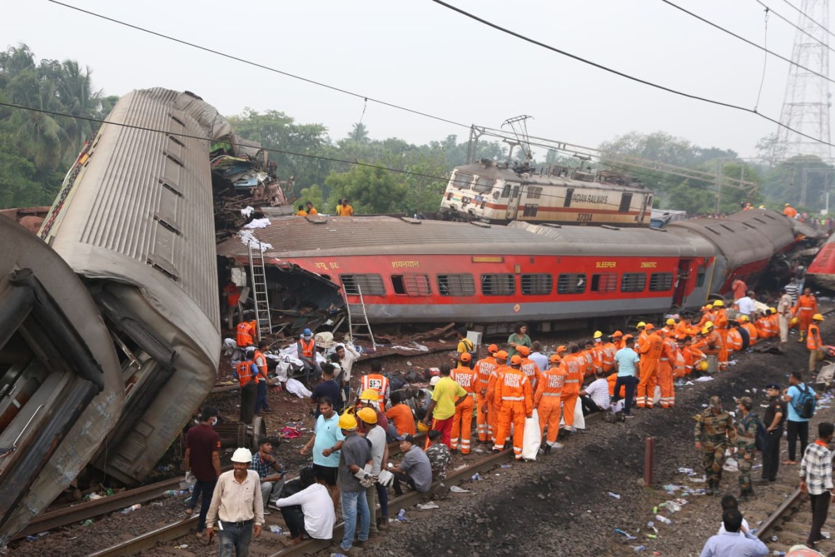 India Railways train crash. A long file of rescue workers in orange construction vests is seen on the tracks next two overturned railway cars.