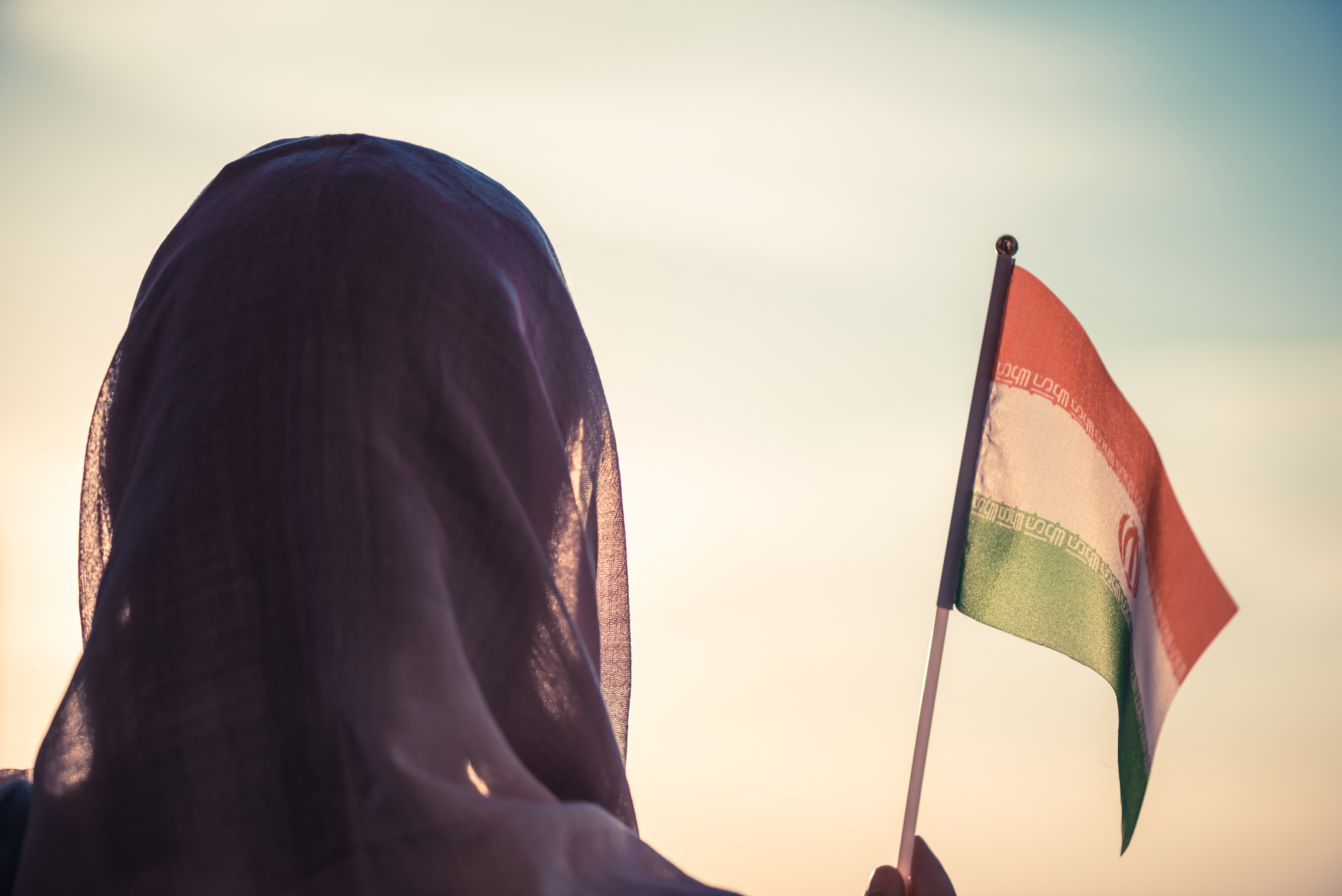 A woman holding an Iranian flag at sunset.