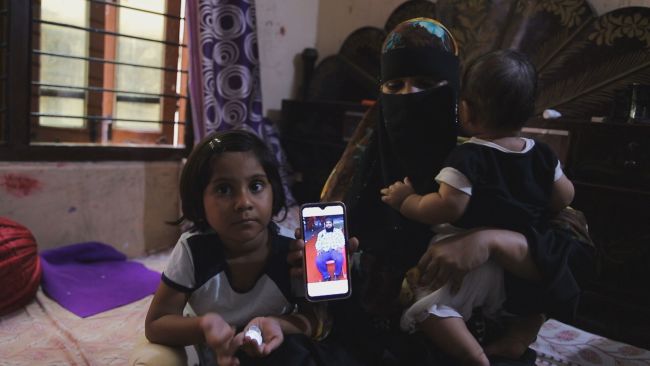 Anjum Shaheen holding a phone picture of her deceased husband, Syed Saifullah, alongside their children.