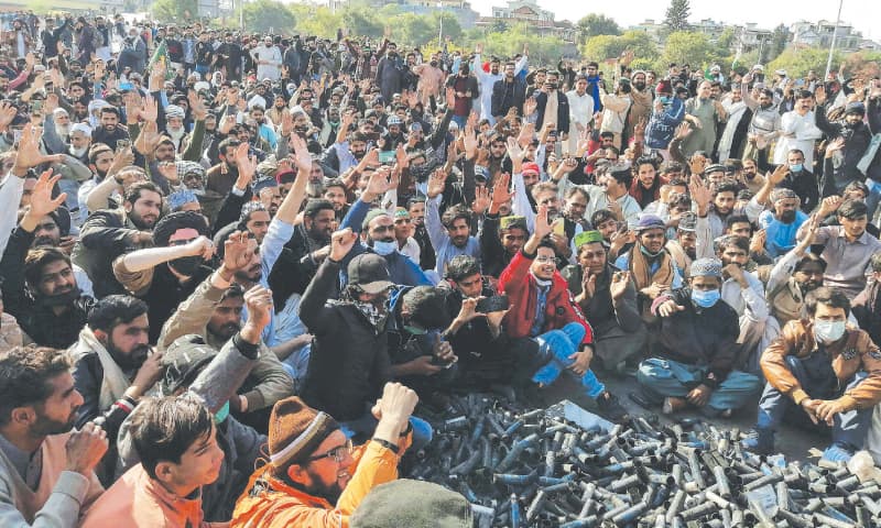 Sitting around empty tear-gas shells fired by the police, TLP supporters shout slogans during an anti-France demonstration. — AFP