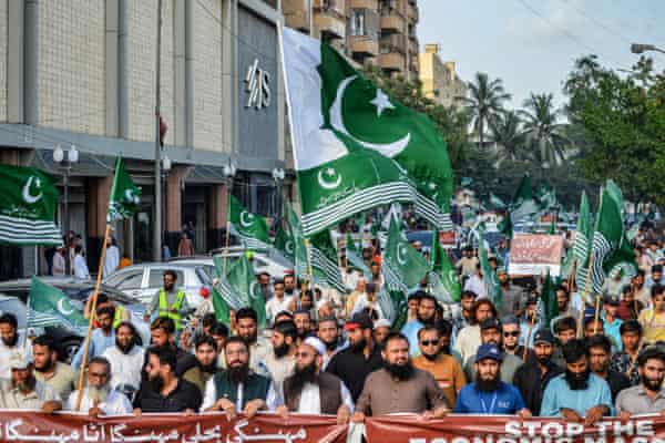 Men with beards march waving placards and green Pakistani-like flags