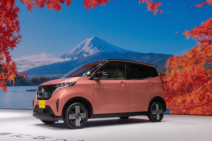 A pink Nissan Sakura against a backdrop of a snow-capped Mount Fuji and red leaves.