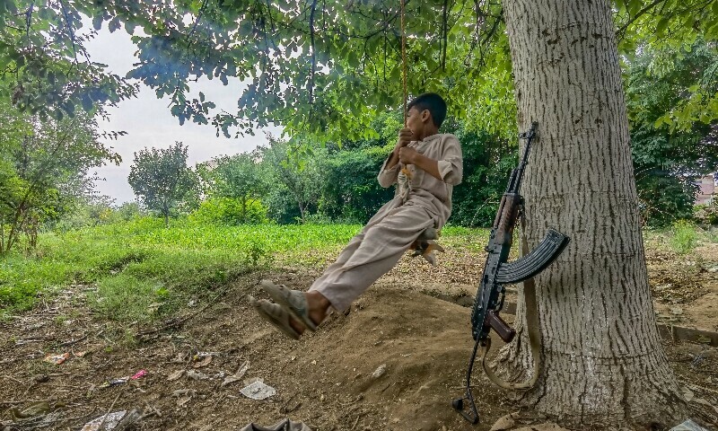 A child swings on a tree as a Kalashnikov lies nearby.