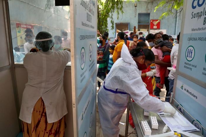 People wait to get tested for Covid-19 in Hyderabad, India. A crowd stands before two health care workers. 