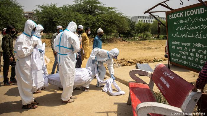 Indian health workers carry a body in a white cowl