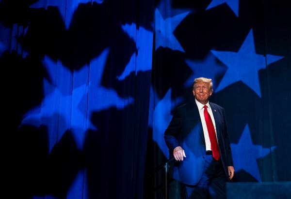 Donald Trump on a stage in front of a blue curtain lit with stars like those on the American flag.