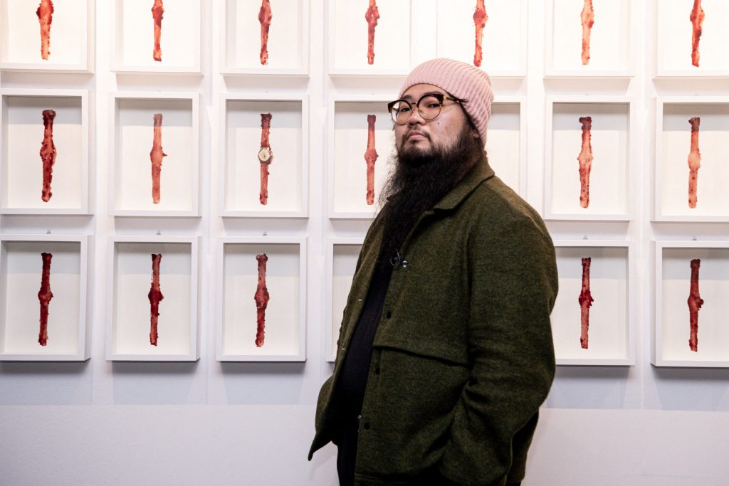 Chinese dissident artist Badiucao poses next to his artwork entitled Watch, 2021 on November 12, 2021 at the exhibition China is (not) near -- works of a dissident artist, opening at the Santa Giulia museum in Brescia, Lombardy. Photo by Piero Cruciatti/AFP via Getty Images.