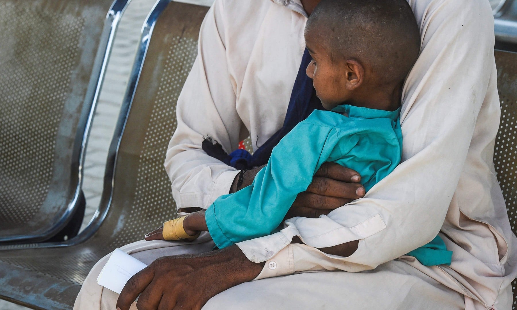 In this picture taken on March 25, a father and his HIV positive son wait for their turn at a treatment support centre in Ratodero. —  AFP