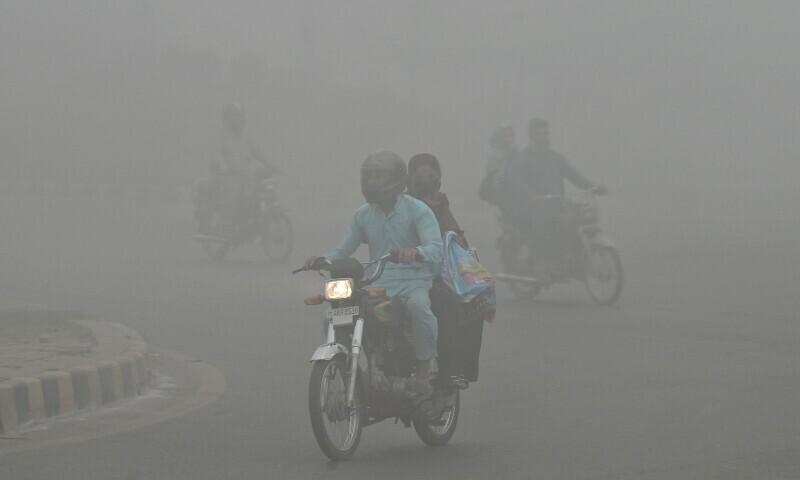 Commuters ride along a road engulfed in thick smog in Lahore on Nov 12, 2024. — AFP