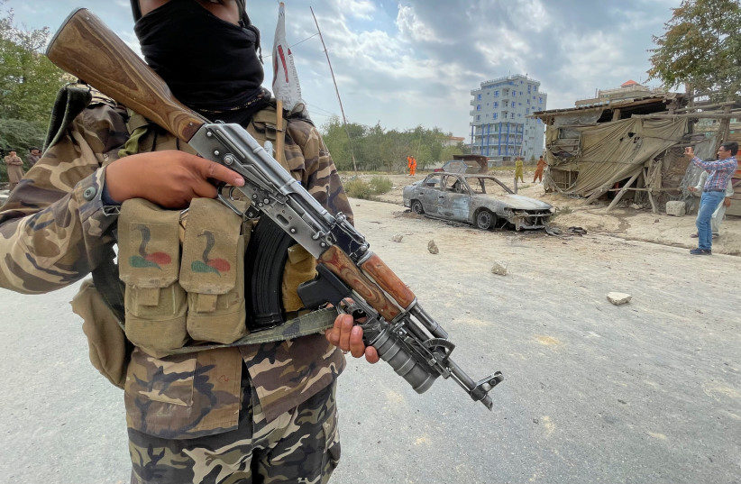  A  TALIBAN member stands guard as Afghan men take pictures of a vehicle from which rockets were fired, in Kabul, Afghanistan, August 30. (credit: STRINGER/ REUTERS)