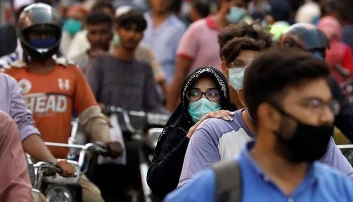 A woman wearing mask pillion rides with a man amid several other motorcycles on a road. Photo: Geo.tv/ file