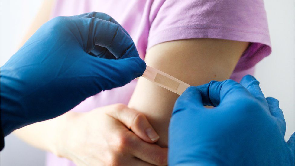 A vaccinator applies an adhesive bandage to a girl after shot