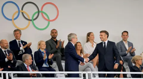  Martin Divíšek/EPA A smiling French President Emmanuel Macron (R) shakes hands with IOC president Thomas Bach as they take their seats in the Trocadero