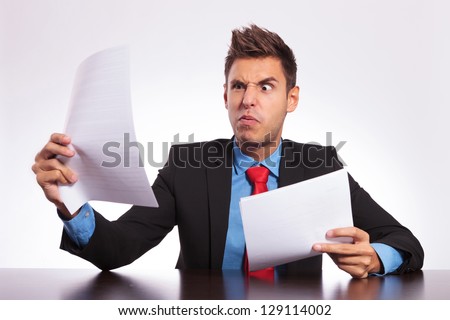 stock-photo-young-business-man-at-the-table-reading-something-unbelievable-and-making-a-weird-face-129114002.jpg