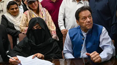 Getty Images Pakistan's former Prime Minister, Imran Khan (R) along with his wife Bushra Bibi (L) looks on as he signs surety bonds for bail in various cases, at a registrar office in the High court, in Lahore on July 17, 2023