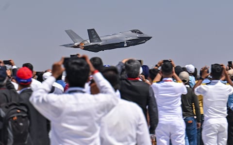Spectators watch as a US Air Force's (USAF) fifth-generation supersonic multirole F-35 fighter jet flies past during a flying display on the second day of the 14th edition of Aero India 2023