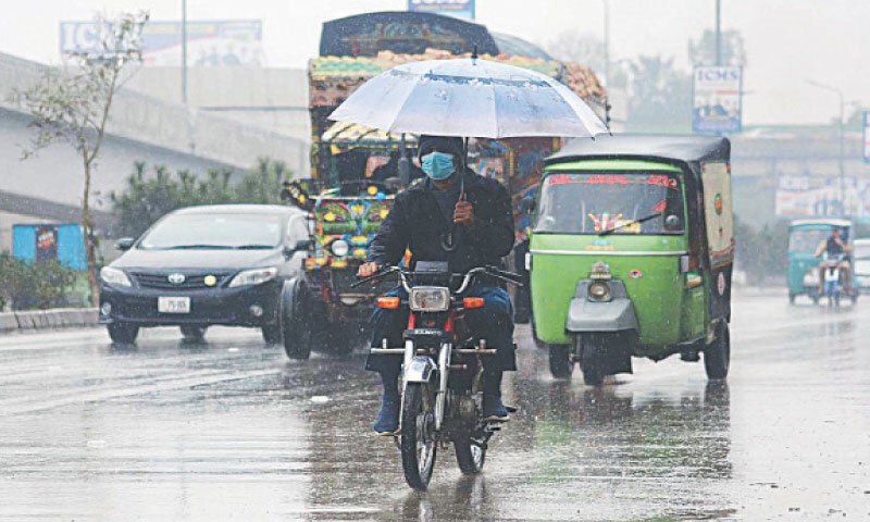 A biker holding an umbrella during rain in Peshawar on Monday. — APP