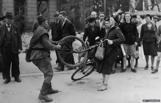 A Soviet soldier struggles to take a woman's bicycle in Berlin