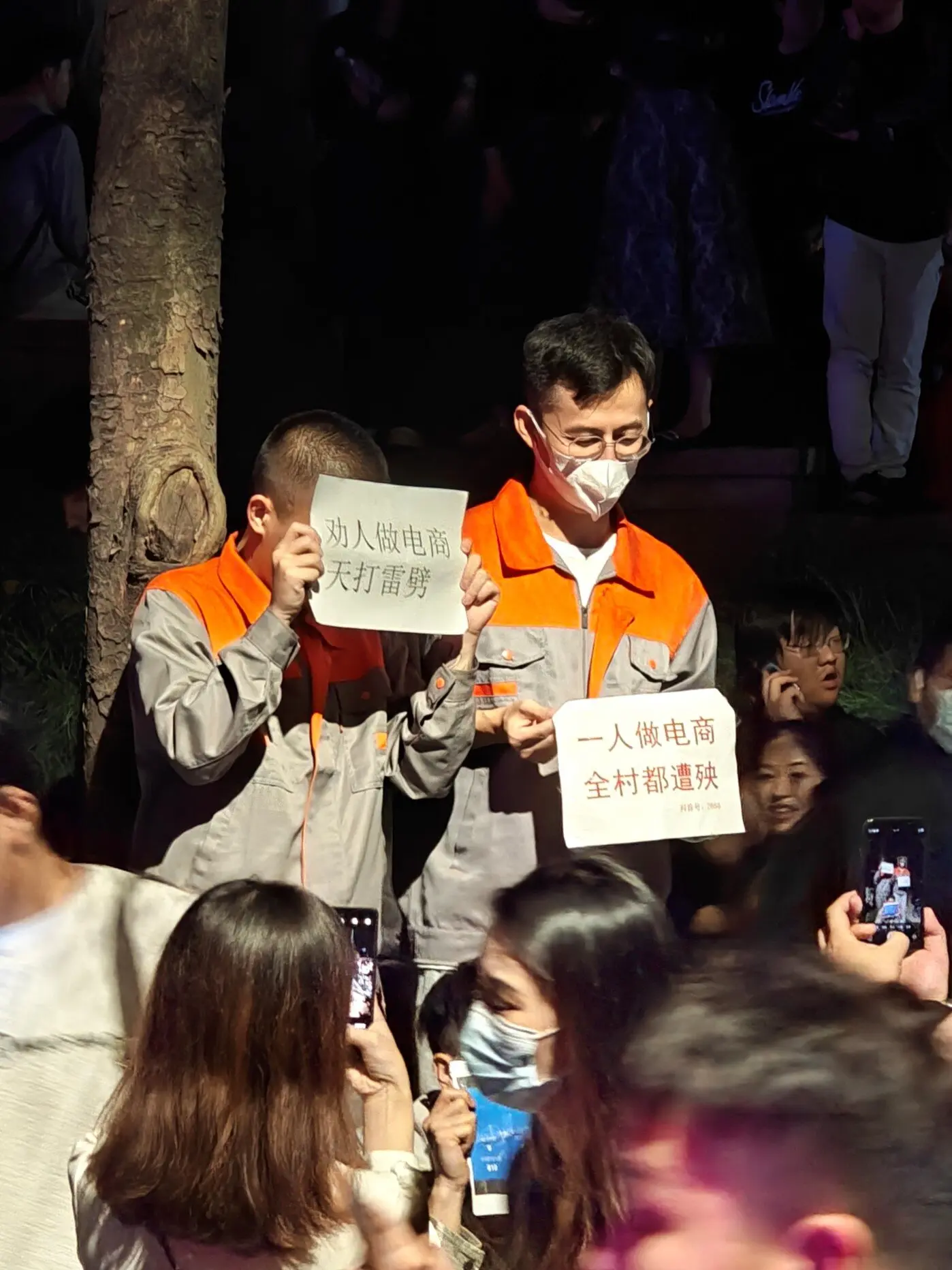 Two men dressed as e-commerce workers standing in front of a crowd holding signs.