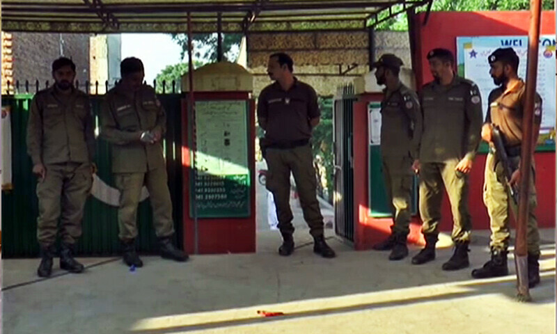 Police personnel stand guard outside a polling station in Faisalabad on Sunday.—DawnNewsTV