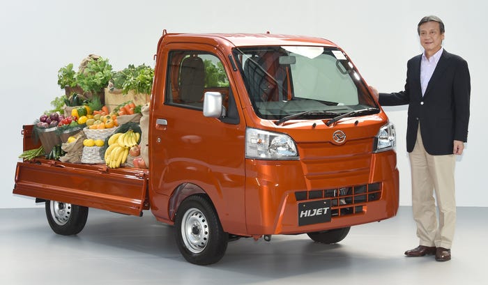 A man standing next to the Daihatsu Hijet mini truck, the trailer of which is filled with baskets of fresh produce.