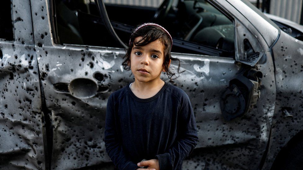 A boy stands next to a car that was damaged by rocket shrapnel in Sderot, Israel (2 May 2023)