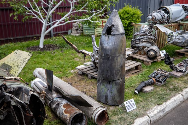a-beaten-up-grayish-cylinder-with-a-conical-top-that-shows-a-large-puncture-mark-stands-on-the-grass-in-a-yard-that-is-strewn-wi.jpg