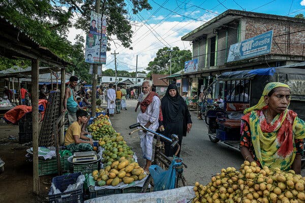 People walk near vendors lining a street, selling fruit. 