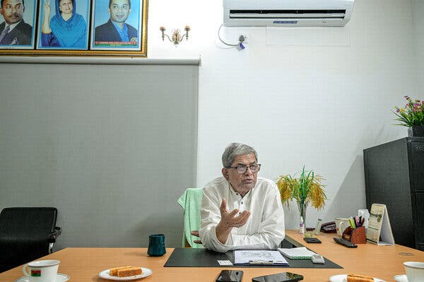 Mirza Fakhrul Islam Alamgir sits at a desk and raises his right hand. A pastry sits nearby on a plate.