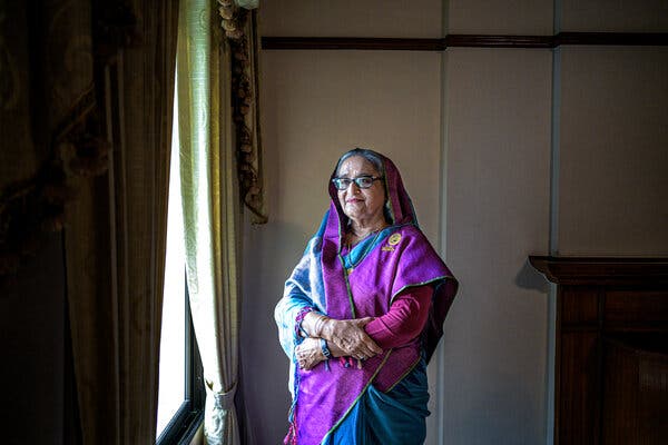 Prime Minister Sheikh Hasina wears a purple and blue outfit as she stands near a window.