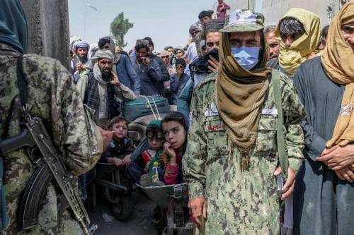 Taliban members stand next to people rushing to pass to Pakistan from the Afghanistan border in Spin Boldak on September 25, 2021